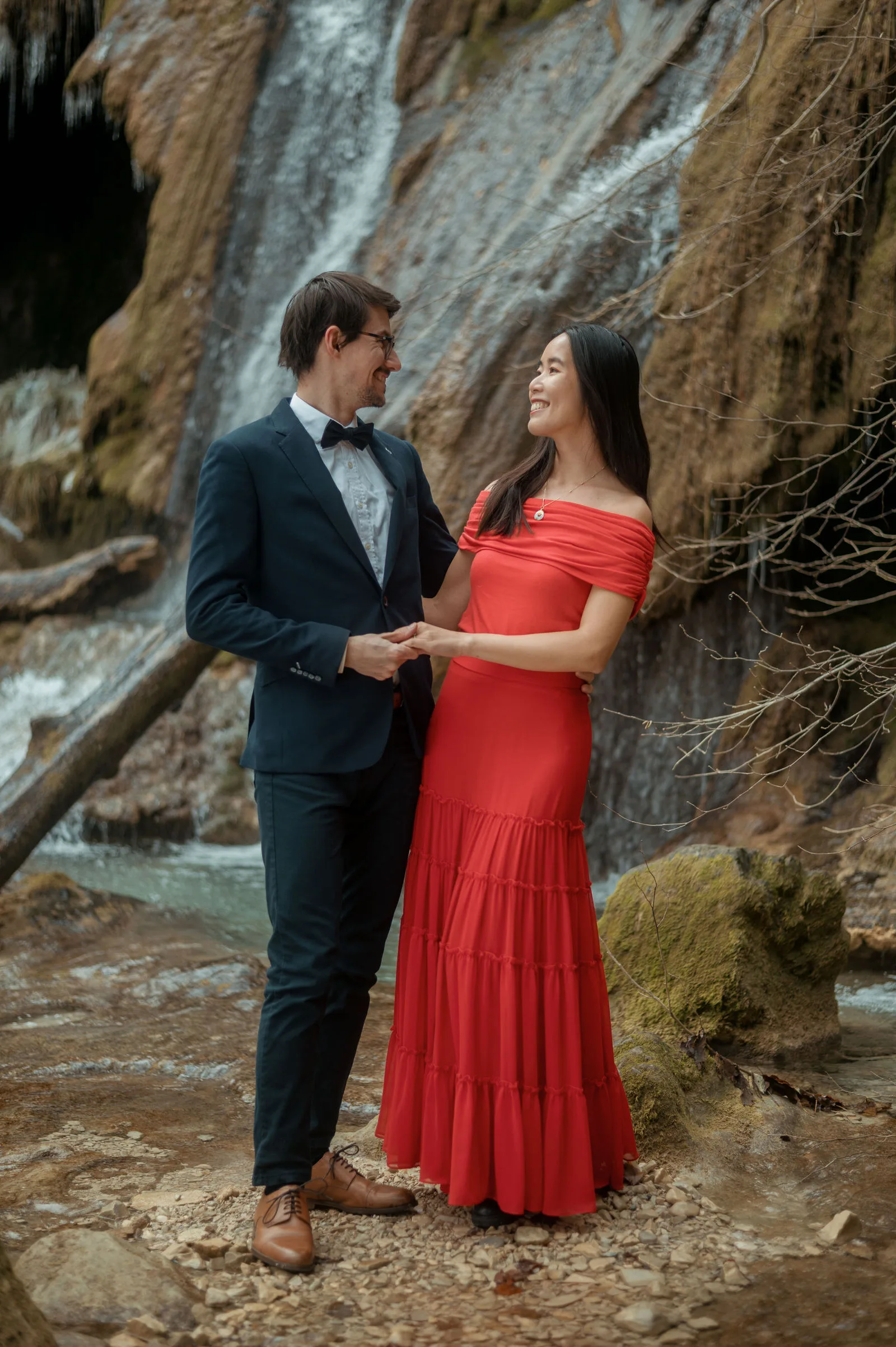 Le couple élégamment habillé devant une cascade en pleine nature lors de la séance d'engagement dans l'Ain