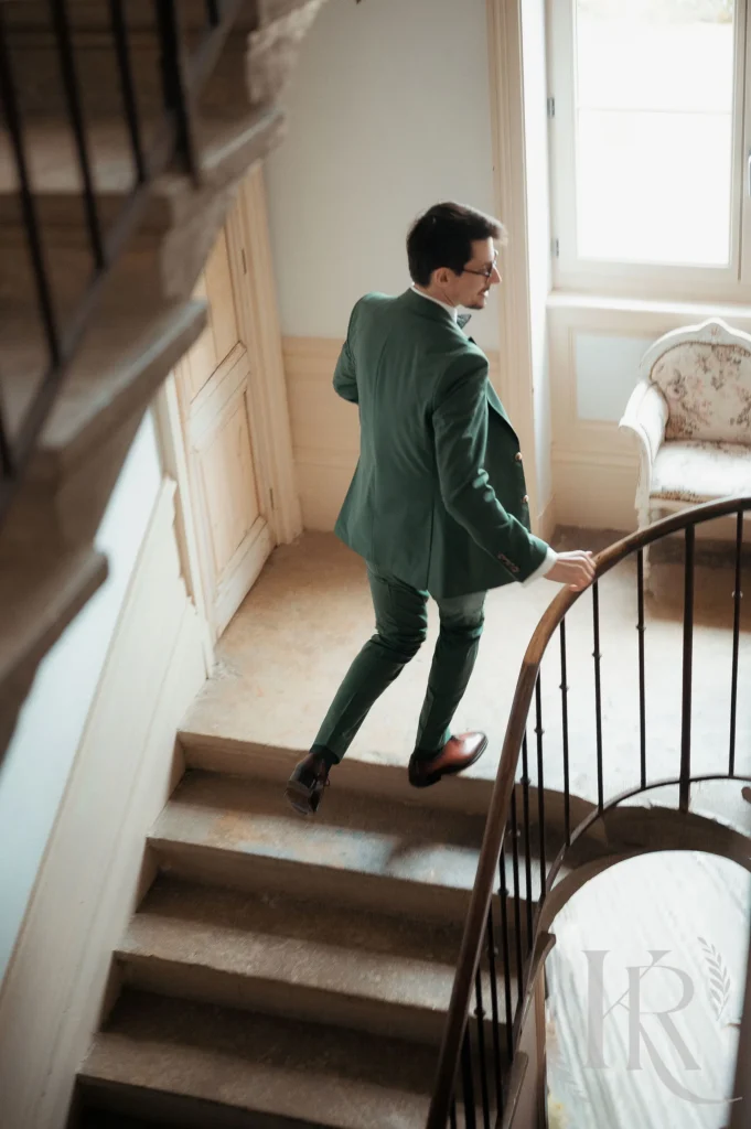 Marié en costume vert descendant un escalier en pierre, photographiée de haut lors d'une séance mariage