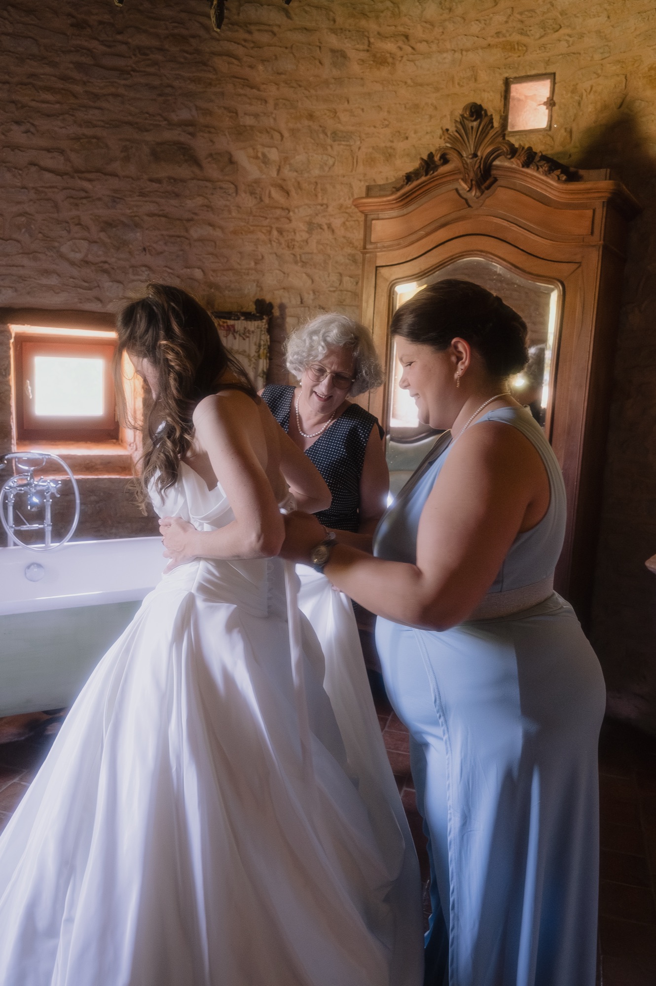 Enfilage de la robe de mariée dans une lumière douce, mariage au Château du Sou, Lacenas